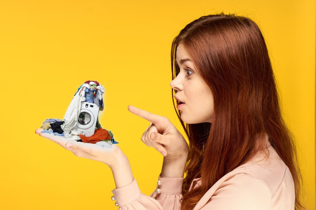 洗濯物の山と洗濯機を指差す女性。家事の大変さをイメージした写真。