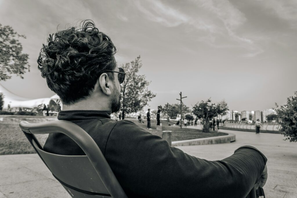 公園のベンチで一人静かに過ごす男性の後ろ姿。気分転換やひとり時間で心をリセットする様子を表す。